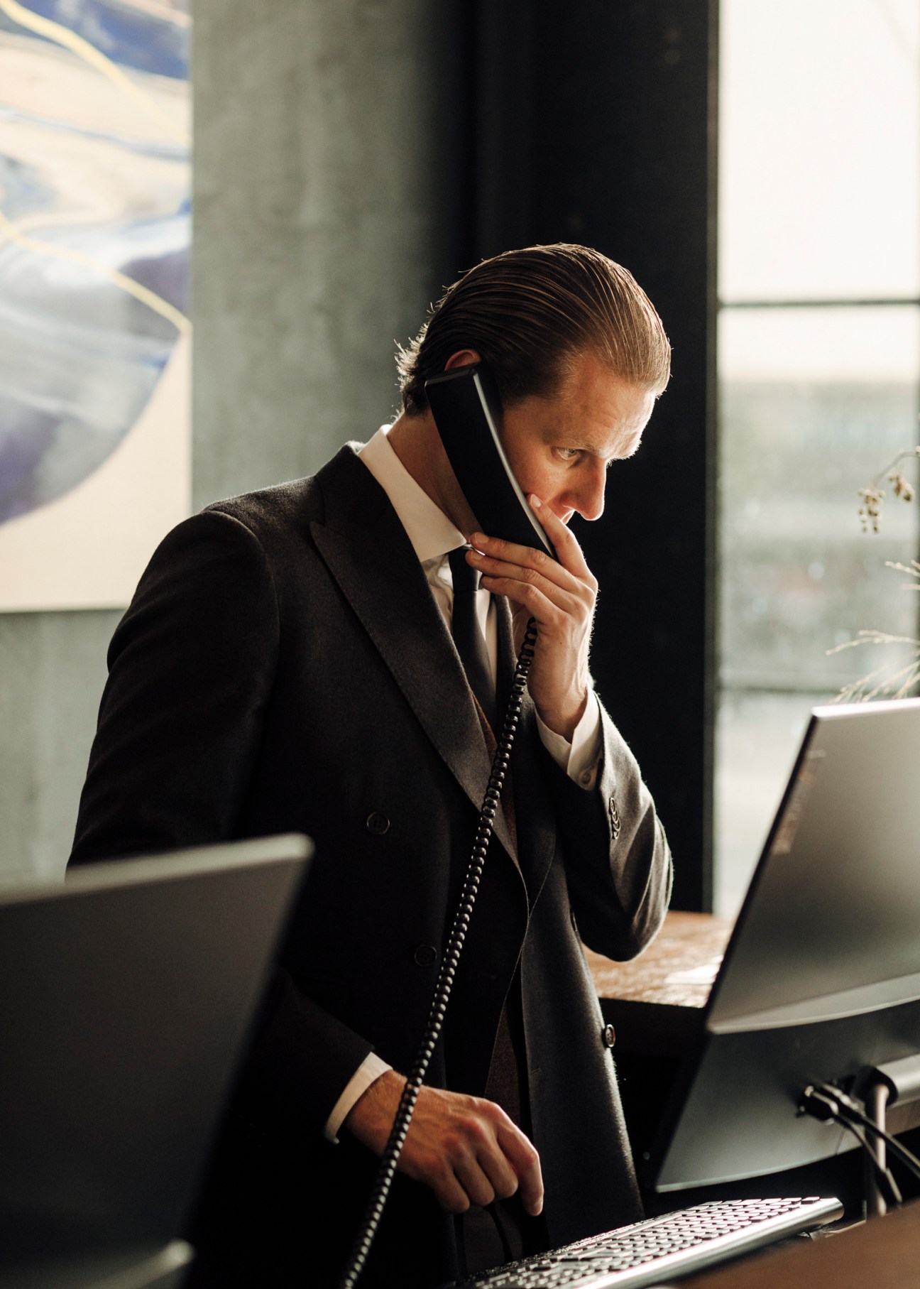 Hotel concierge in dark suit speaking on telephone while working at desk