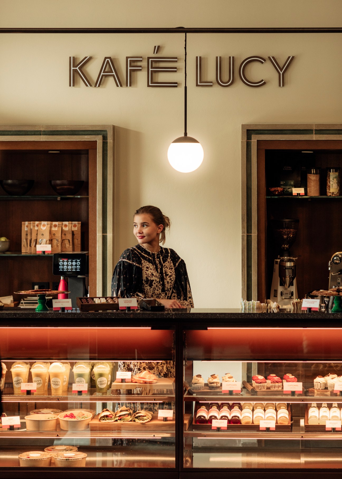 Staff member at Kafe Lucy coffee counter in Sommerro hotel lobby with pastries and coffee service
