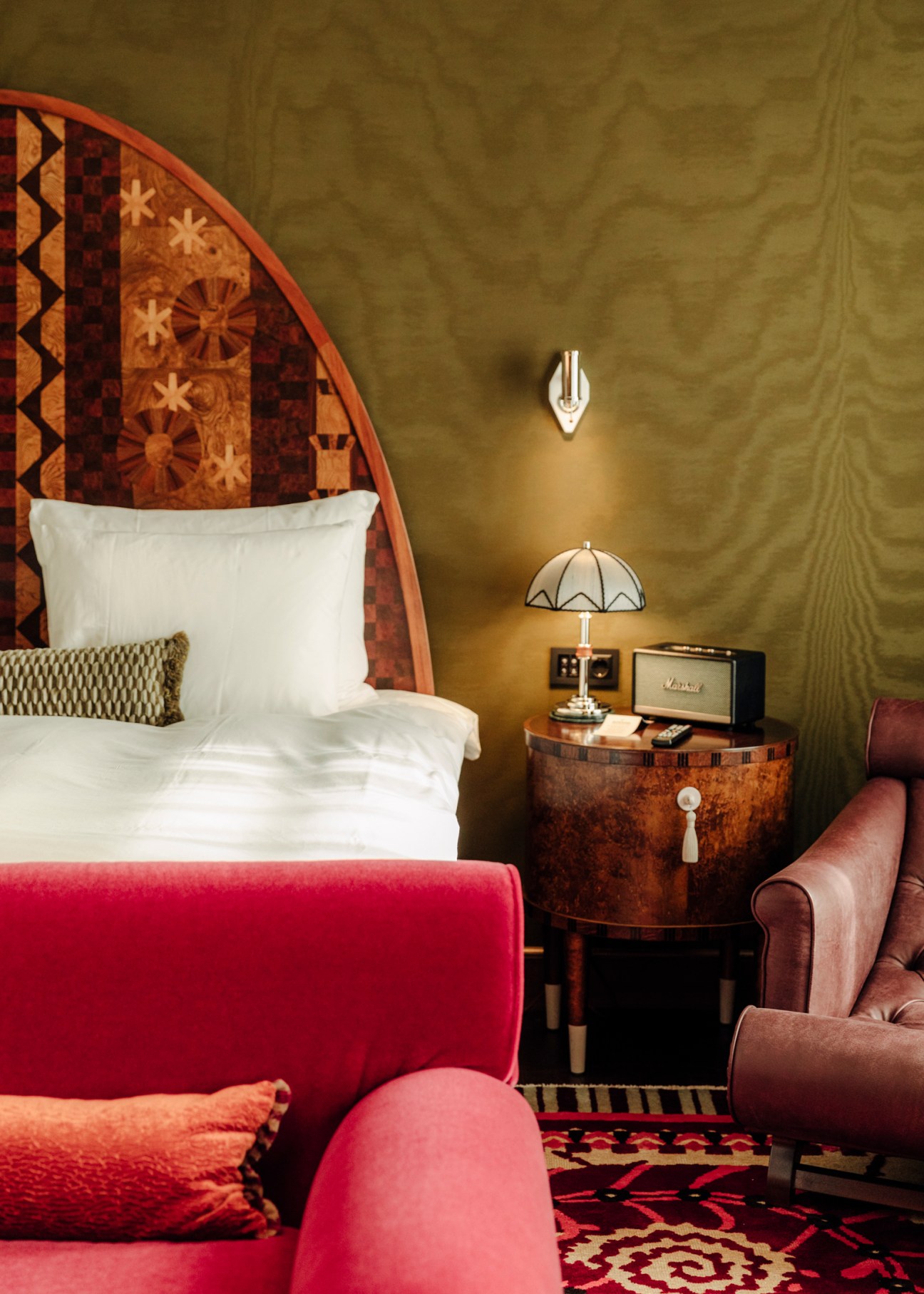 Sommerro hotel bedroom with decorative headboard, vintage radio, red chair, and patterned rug