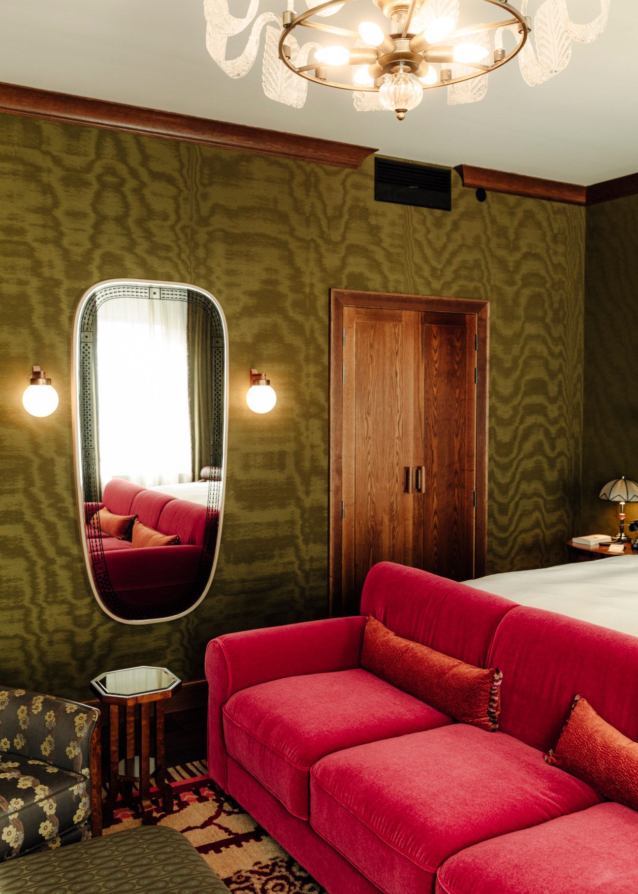 Sommerro hotel suite interior with red velvet sofa, olive green wallpaper, oval mirror and wooden wardrobe