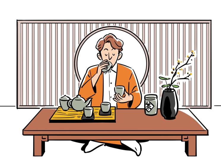 Man in orange cardigan sitting at low table performing Japanese tea ceremony with teapot and cups