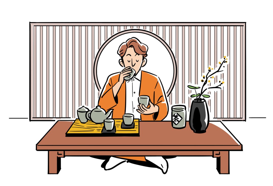 Man in orange cardigan sitting at low table performing Japanese tea ceremony with teapot and cups