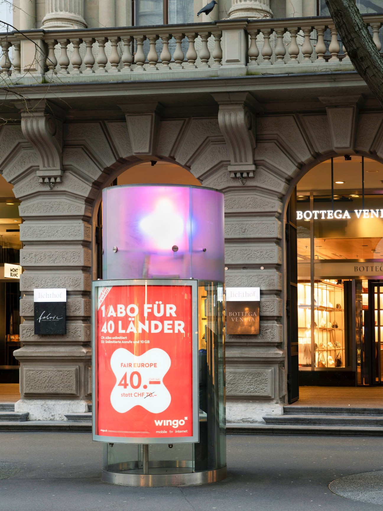 Modern glass telephone booth with digital advertising display on a Zurich street