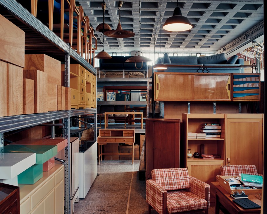 Industrial showroom space with metal shelving, vintage wooden furniture, pendant lights and an orange patterned armchair