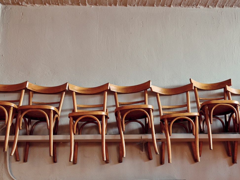 Row of vintage café chairs from the 1950s with wooden seats and curved backs stacked against a white wall