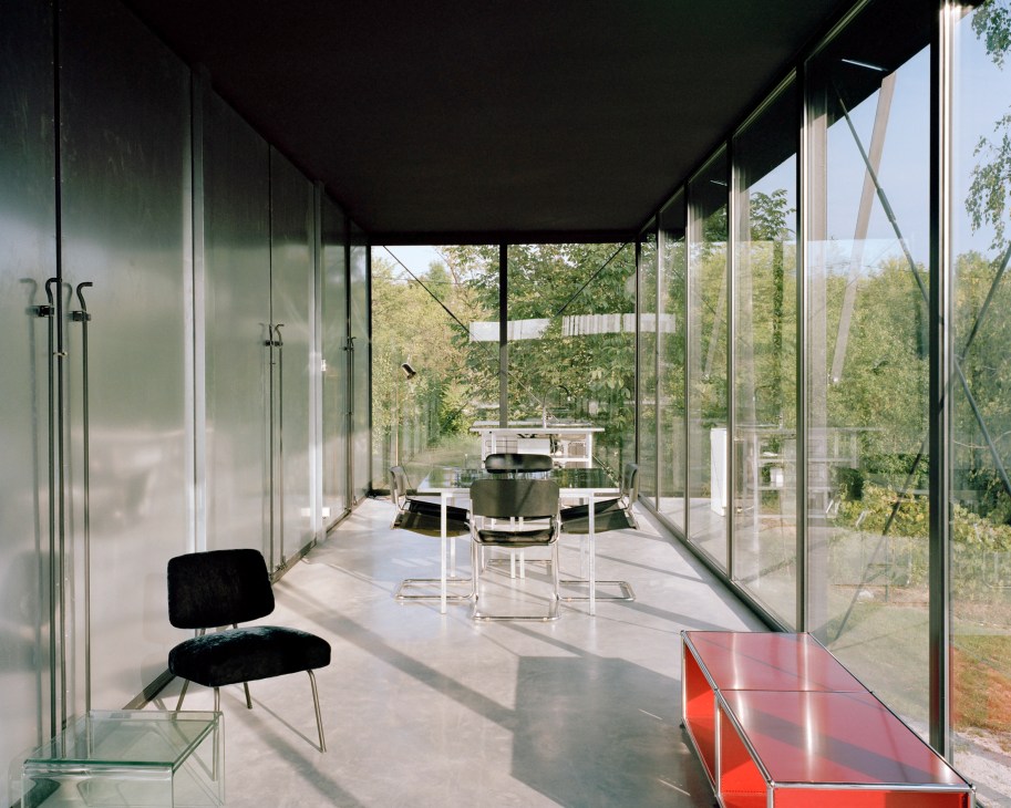 Modern interior of Avala House with floor-to-ceiling windows overlooking forested landscape, minimalist furniture and natural light.