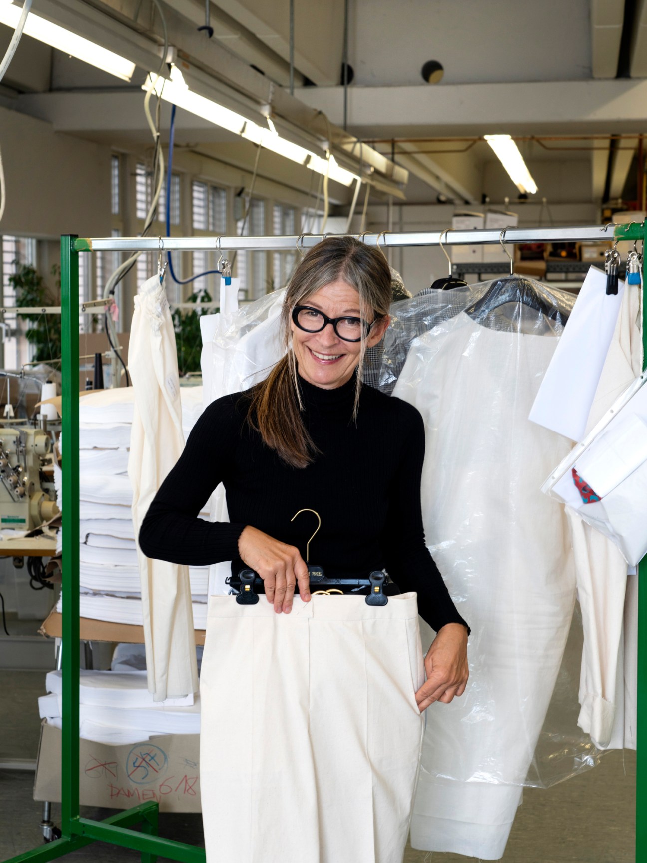 Dorothee Vogel smiling in black top standing behind clothing rack with white garments in factory setting