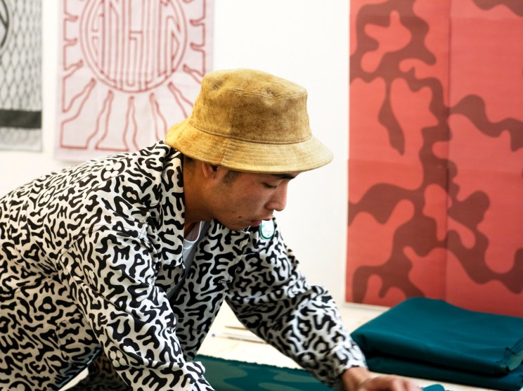 man in a patterned jacket and bucket hat working on a painting.