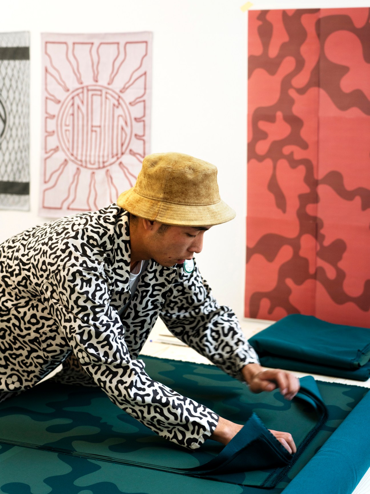 Person in patterned shirt and bucket hat carefully folding and packing blue fabric pieces on a work table