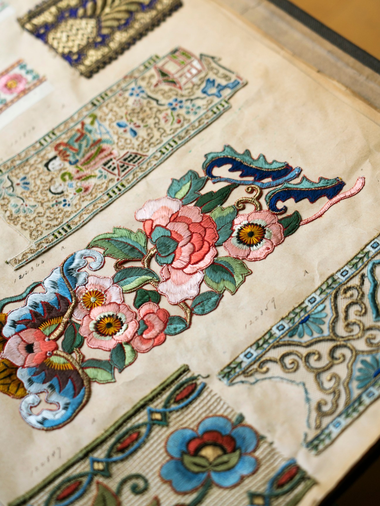 Historical fabric samples with ornate floral embroidery and decorative patterns displayed on aged pages