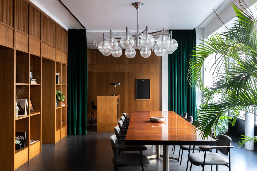 Modern office interior with wooden dining table, metal globe pendant lights, and green curtains.
