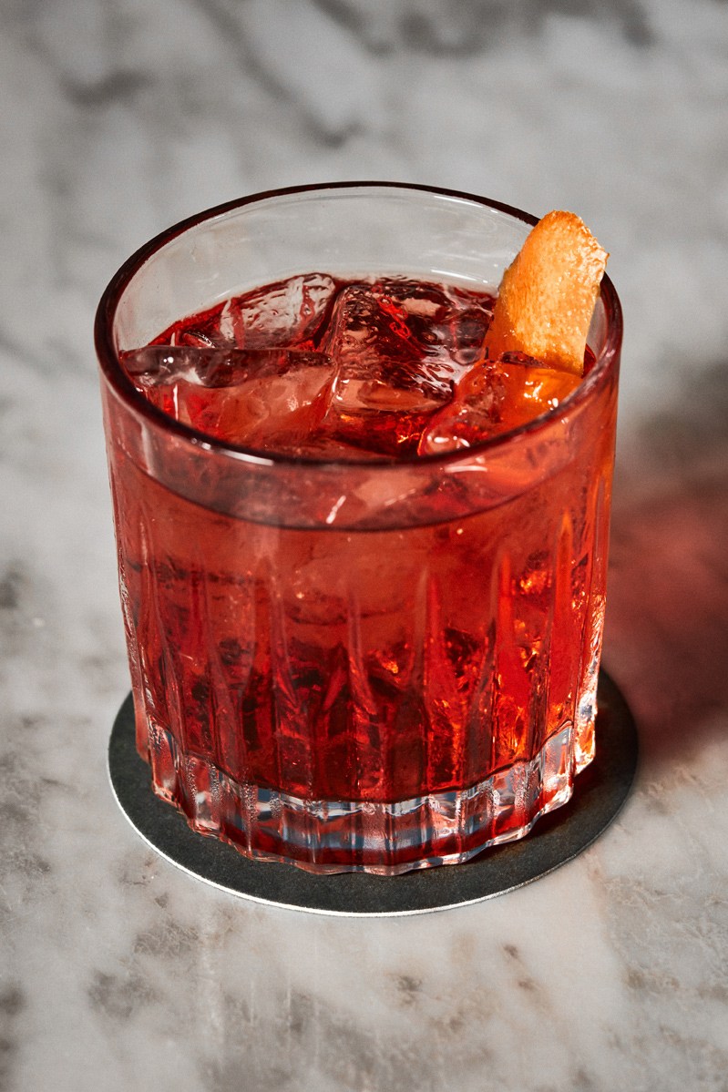 Red cocktail with ice and orange peel garnish in cut crystal glass