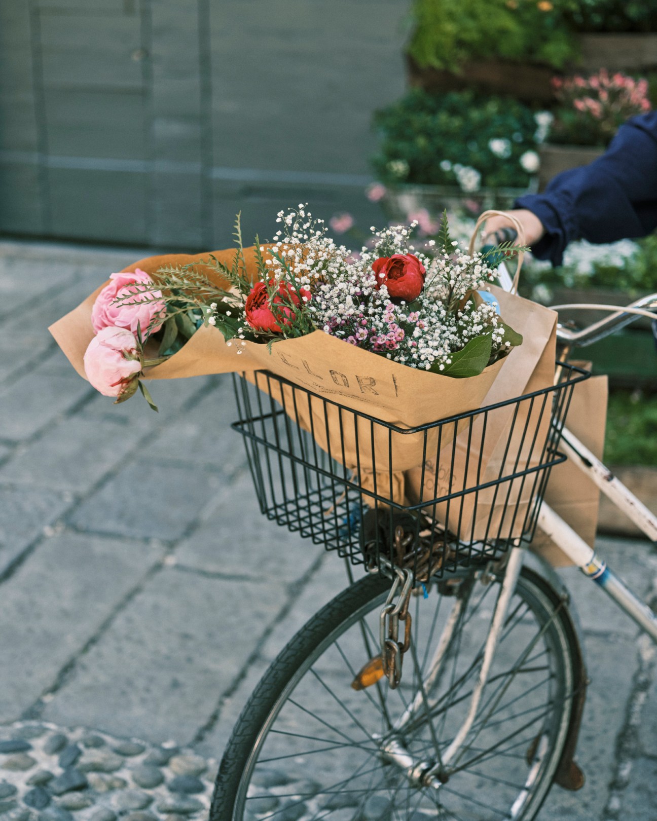 Bicycle basket filled with a bouquet of pink roses, red flowers, white baby's breath and greenery wrapped in kraft paper.