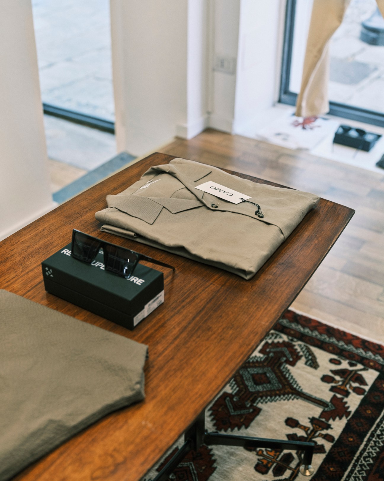 Beige folded garment with brand label and black product box displayed on wooden table in retail shop.