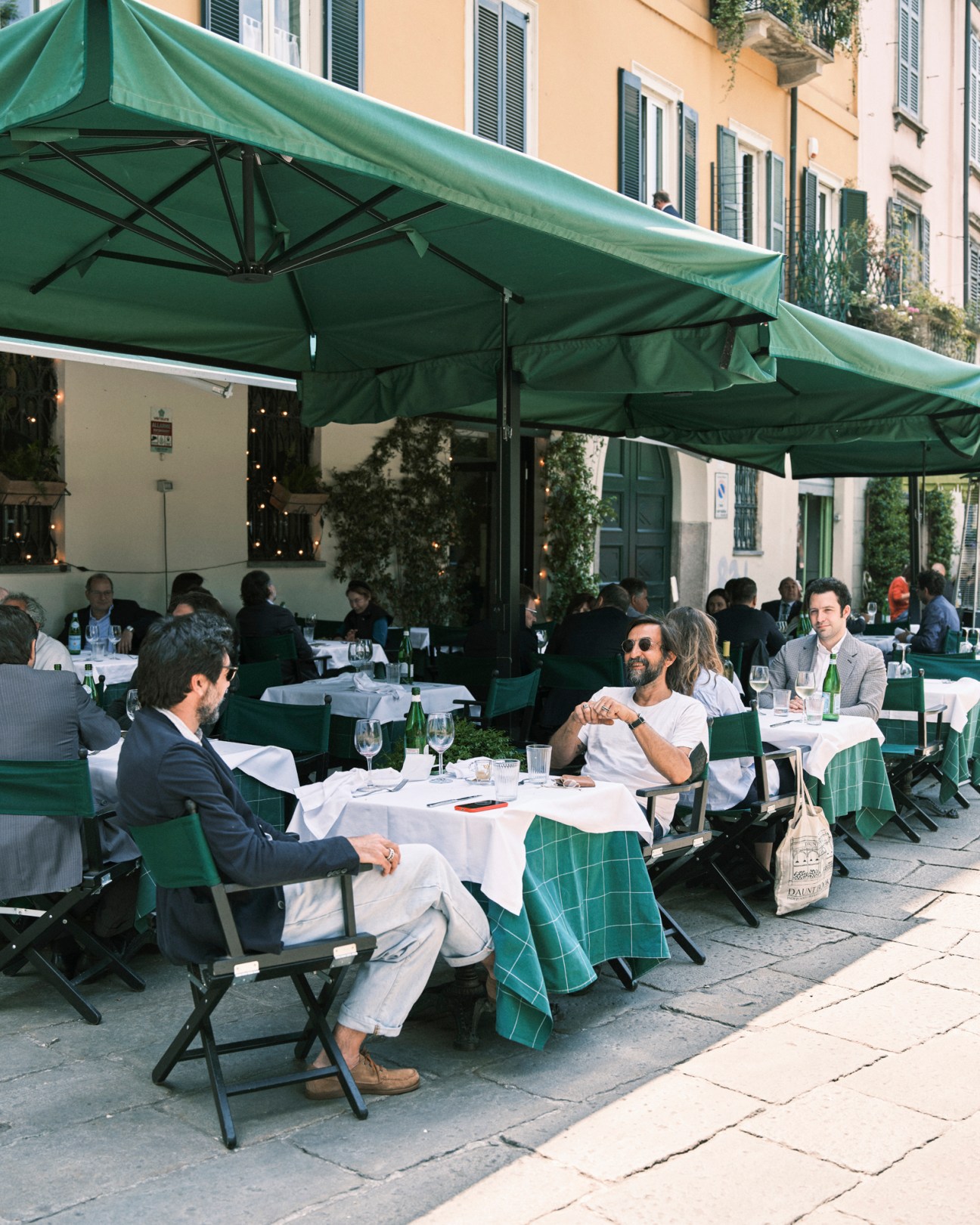 Diners seated at tables under green umbrellas on the outdoor terrace of Sant'Eustorgio restaurant in Milan.