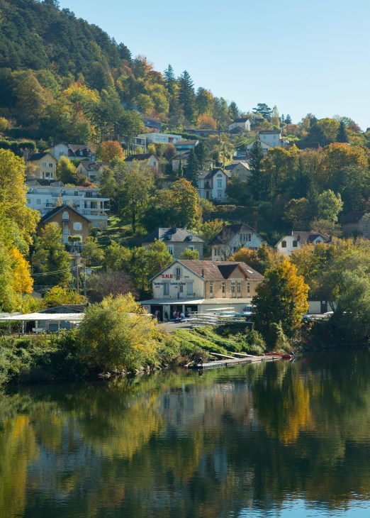 Besançon, France: A riverside town nestled in forested hills with historic buildings and a railway station reflected in the water.