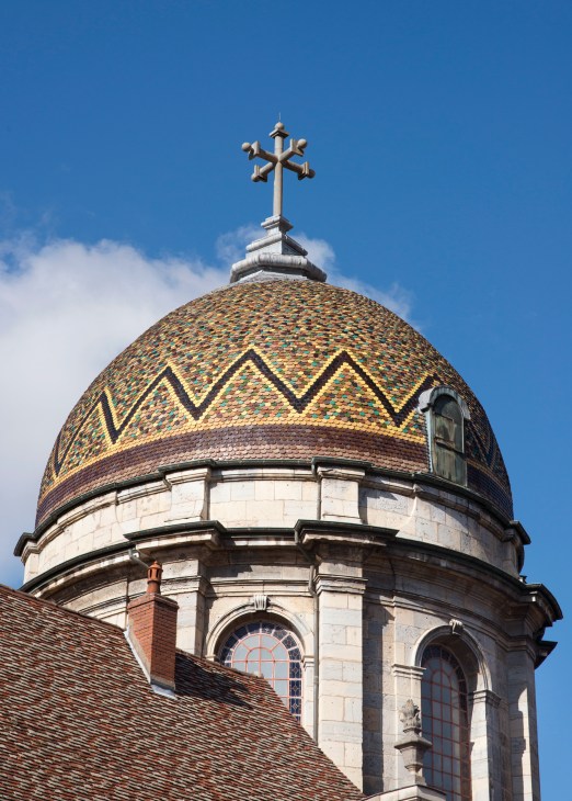 Ornate dome with colorful patterned tiles and golden cross on top against blue sky