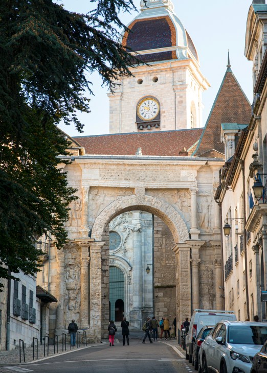 Historic stone church with clock tower in Besançon, France, featuring ornate arched entrance and surrounding traditional buildings.