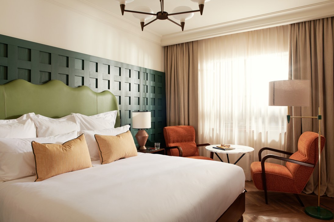 Hotel bedroom with green geometric headboard, white bedding, orange armchairs and modern ceiling fan