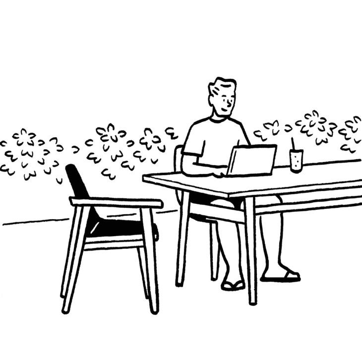 Man working at laptop at outdoor table with empty chair beside him