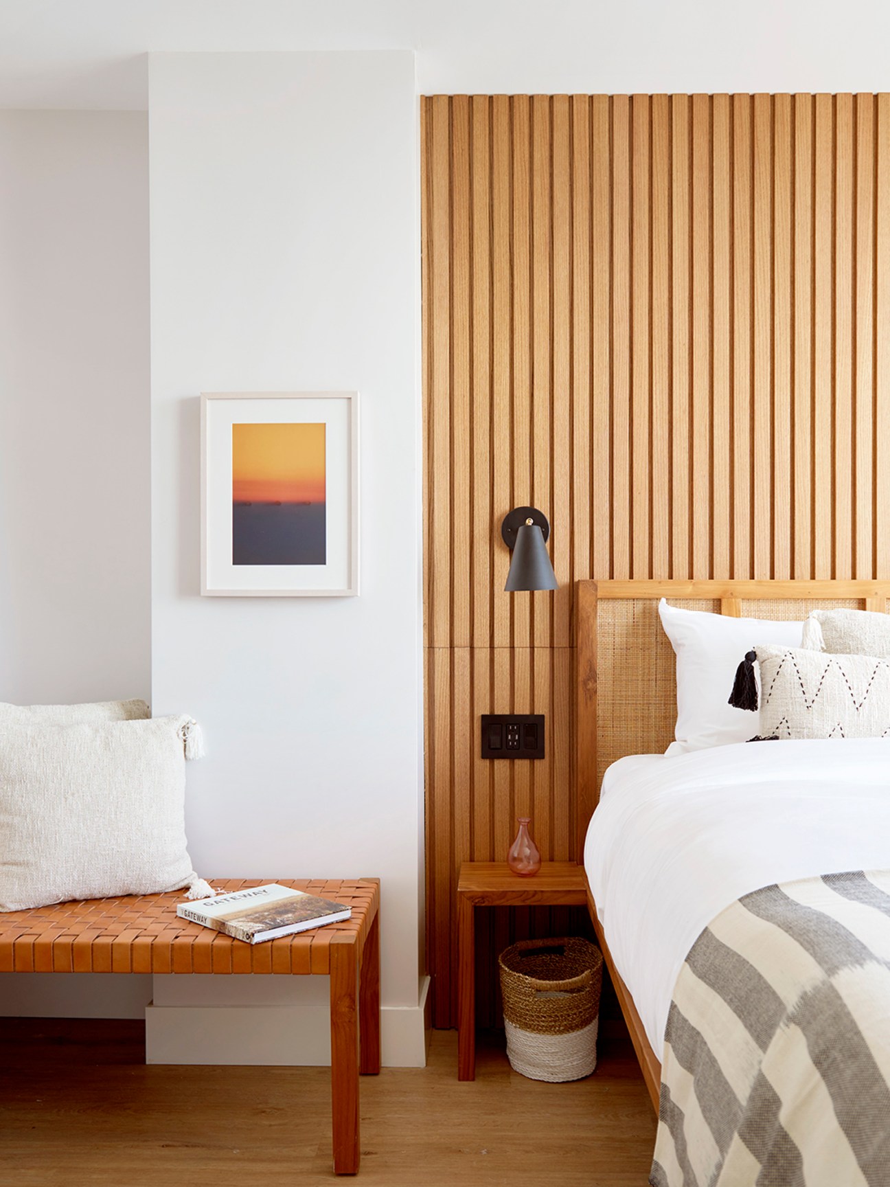Rockaway Hotel guest room with wooden bed frame, white bedding, woven bench, and framed sunset artwork.