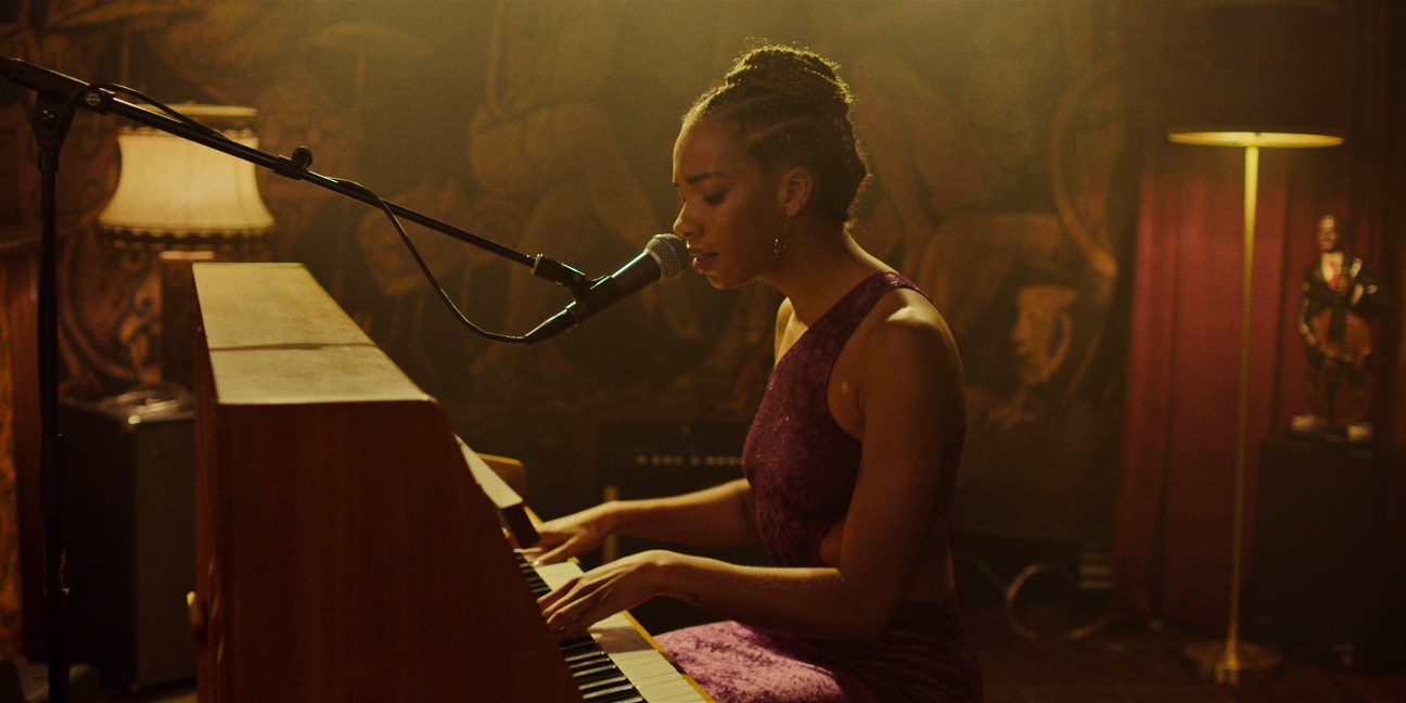 Woman singing into microphone while playing piano in dimly lit intimate venue