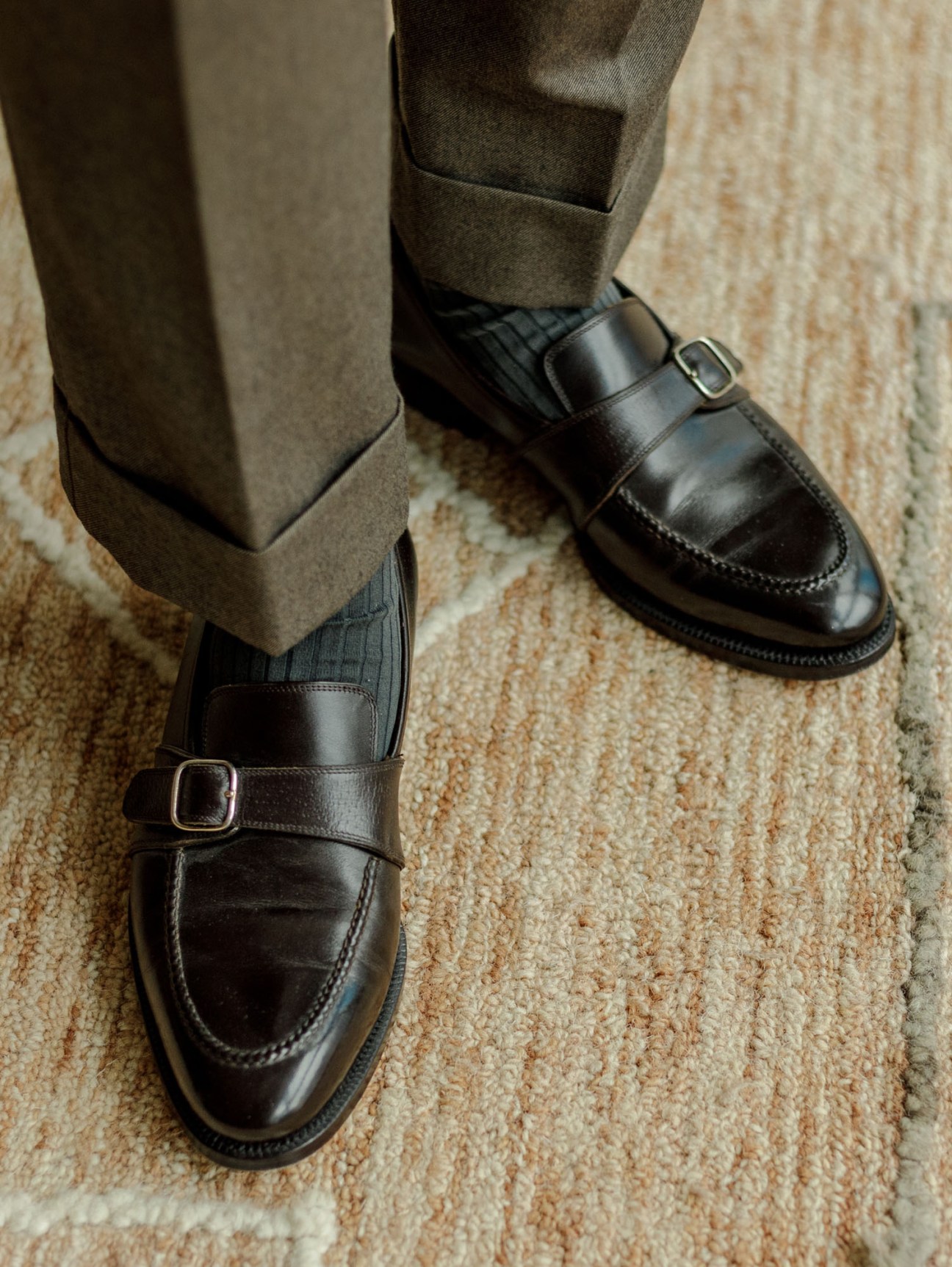 Close-up of black leather loafers with buckle straps and striped socks on beige carpet