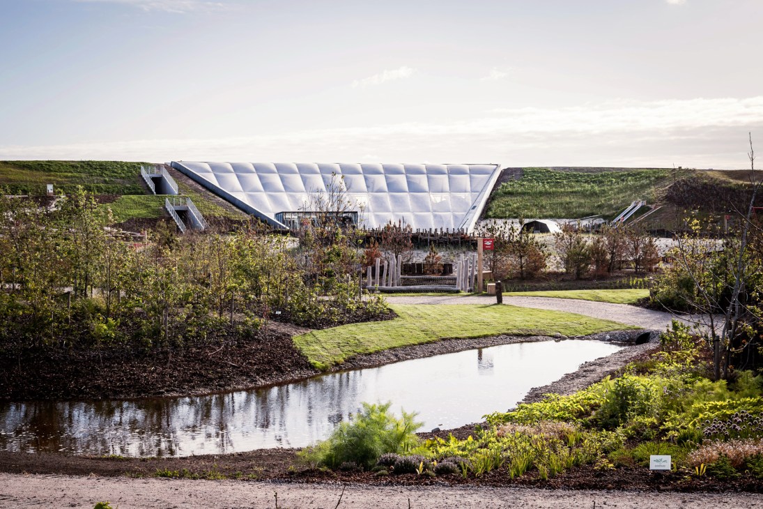 Modern white angular building with geometric roof integrated into green landscape at Naturkraft