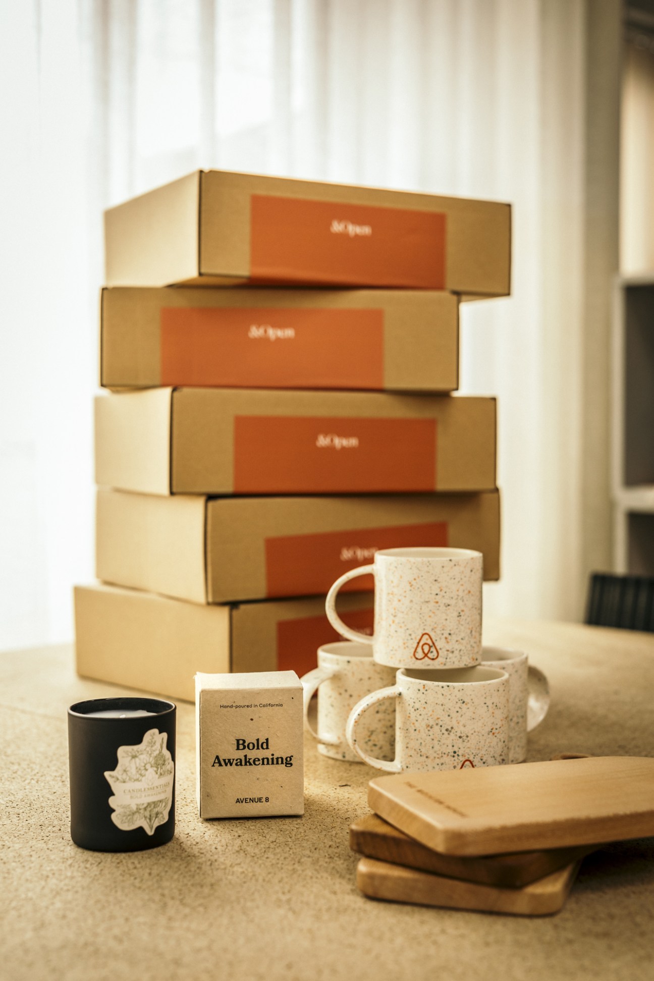 Stack of cardboard shipping boxes with orange labels next to coffee mugs and wooden coasters on counter