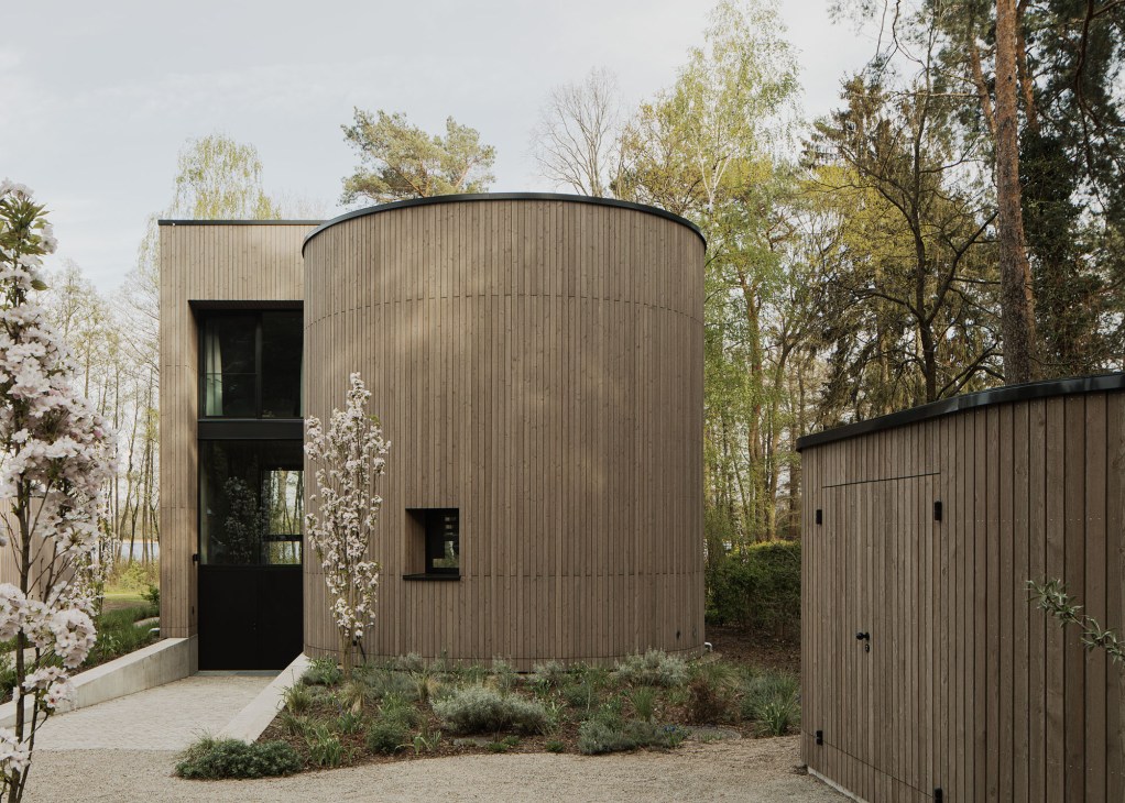Modern timber house with vertical wood cladding and large windows nestled among tall trees in a forest setting