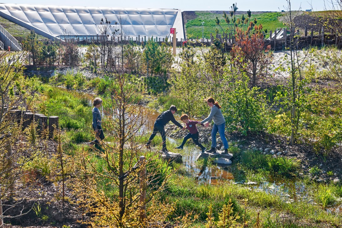 Children playing on stepping stones across water stream at Naturkraft nature playground in Denmark