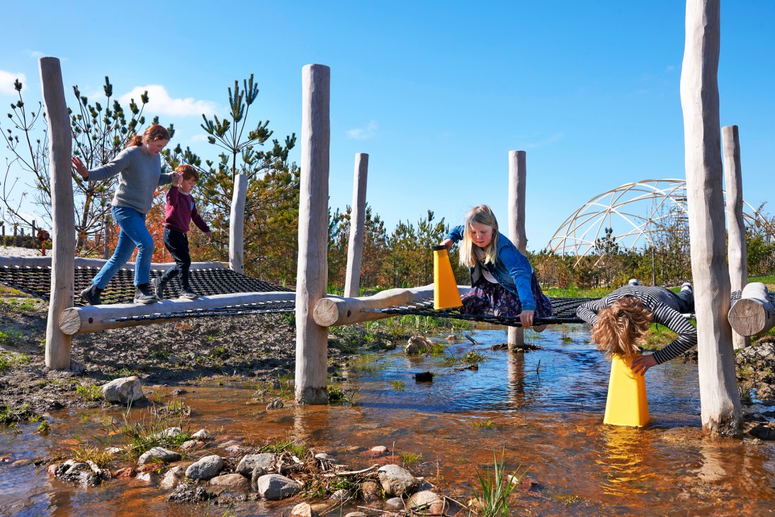 Children playing on rope nets and exploring water features at Naturkraft nature playground in Denmark