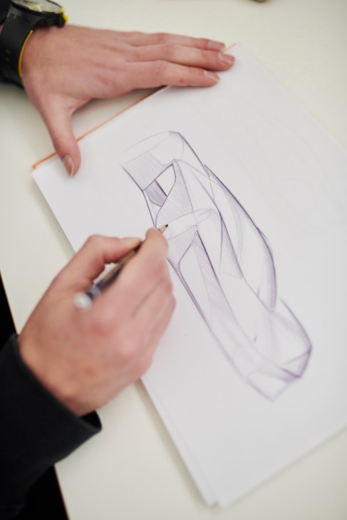 Designer's hands sketching a vehicle design on white paper with pencil.