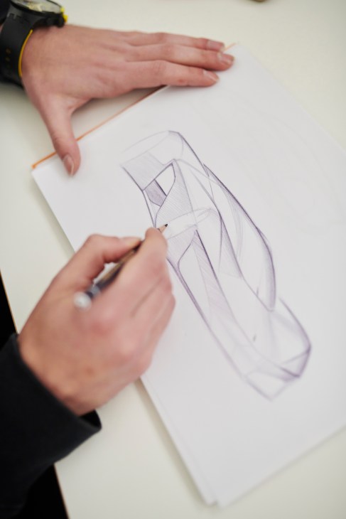 Designer's hands sketching a vehicle design on white paper with pencil.