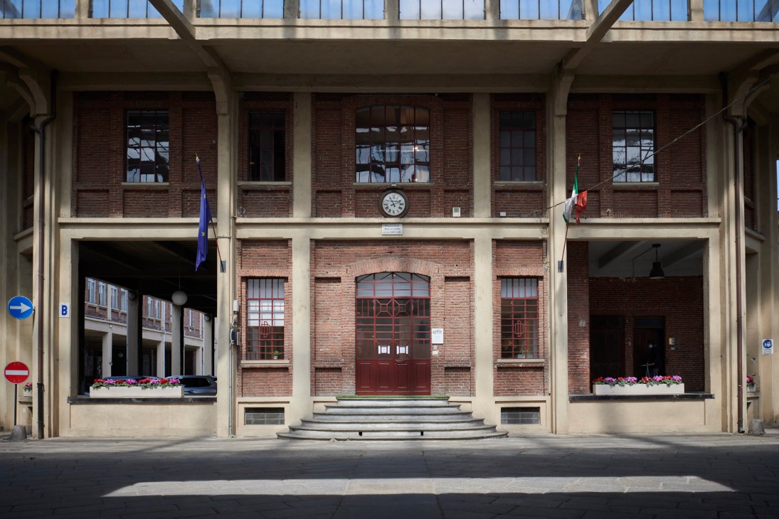 Red brick industrial building with concrete columns and Italian flag, housing Cingomma in Turin's Docks Dora warehouse.