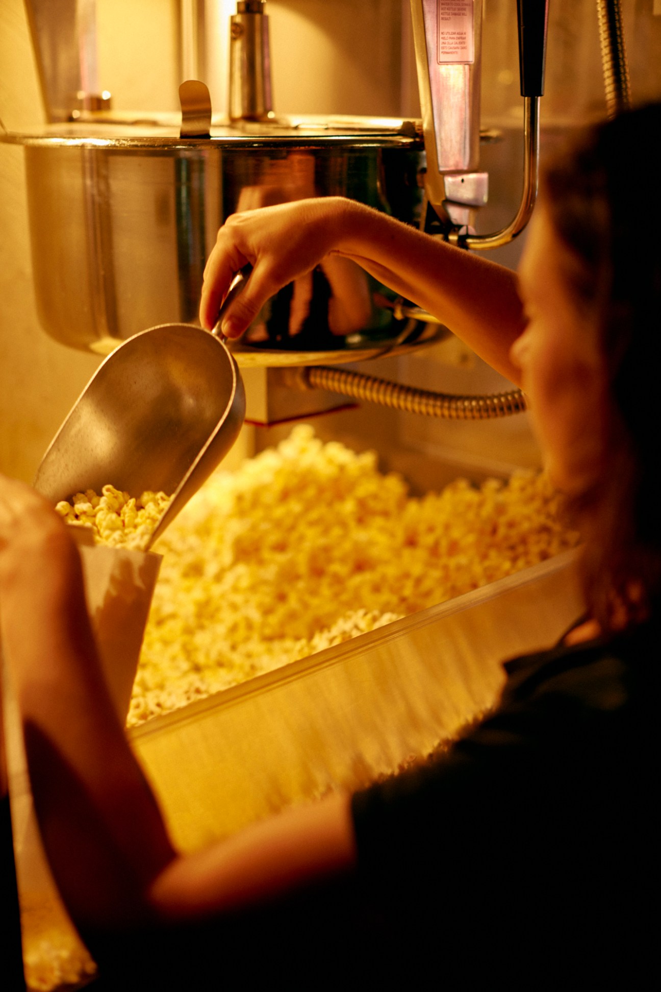 Hand scooping freshly popped popcorn from commercial cinema popcorn machine with metal scoop