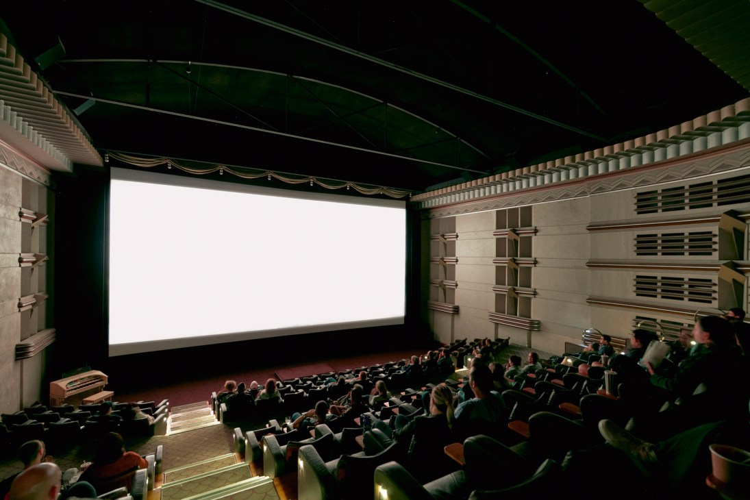 Interior view of a cinema screening room with audience seated watching a blank white screen
