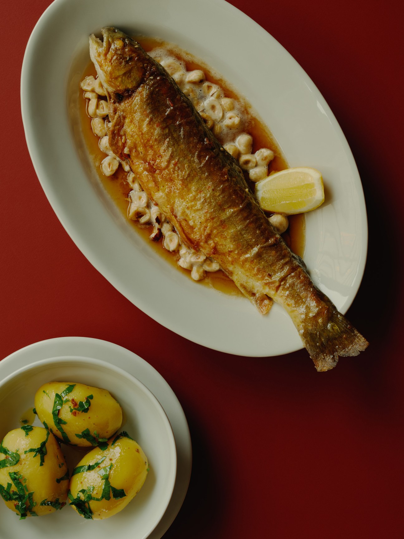 Whole trout Müllerin served on white oval plate with brown prawns and lemon wedge