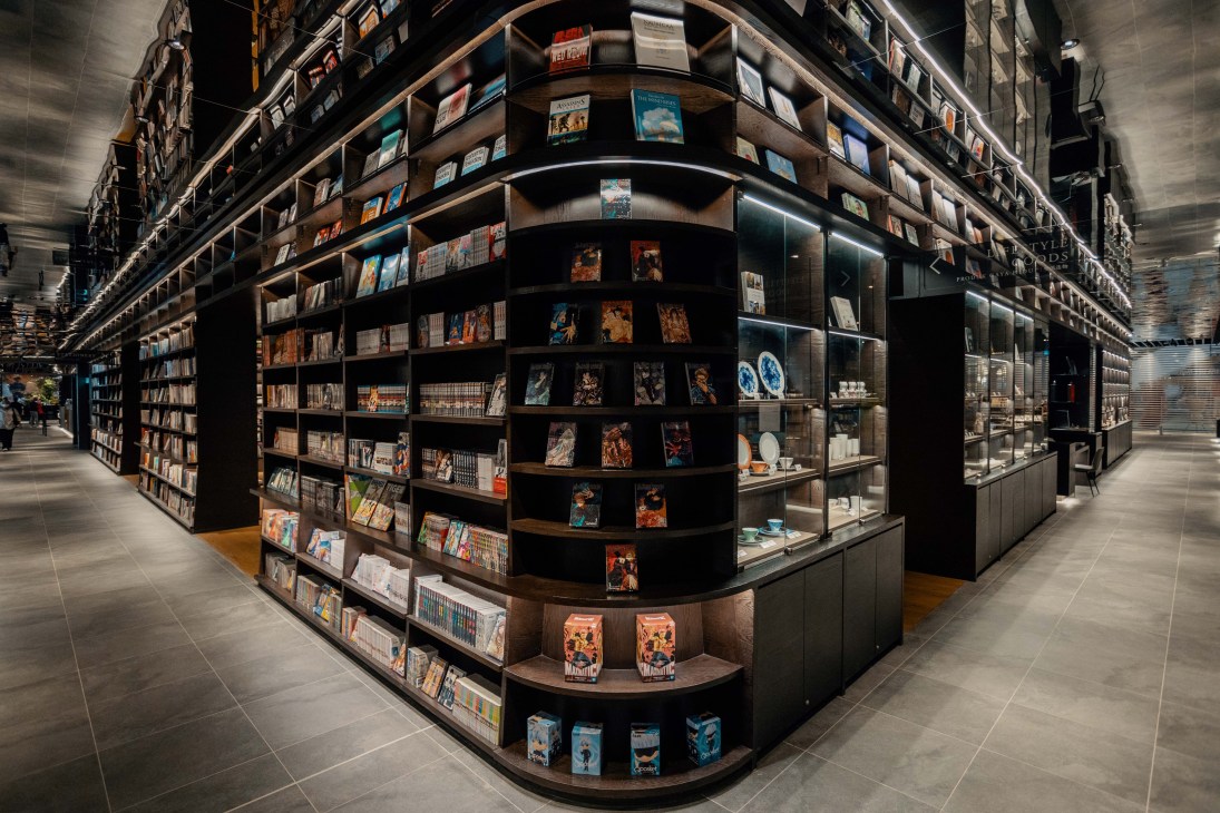 Modern bookstore interior with curved shelving displays filled with books and magazines under warm lighting