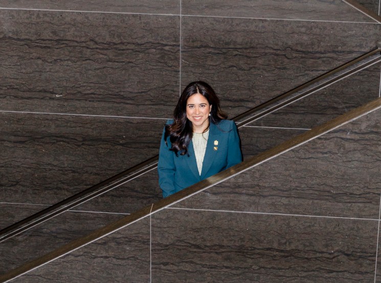 Woman in navy blazer standing on modern stone staircase in contemporary building interior.