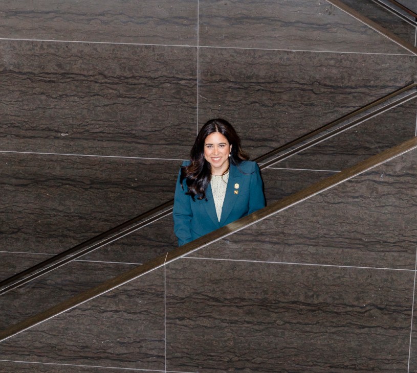 Woman in navy blazer standing on modern stone staircase in contemporary building interior.