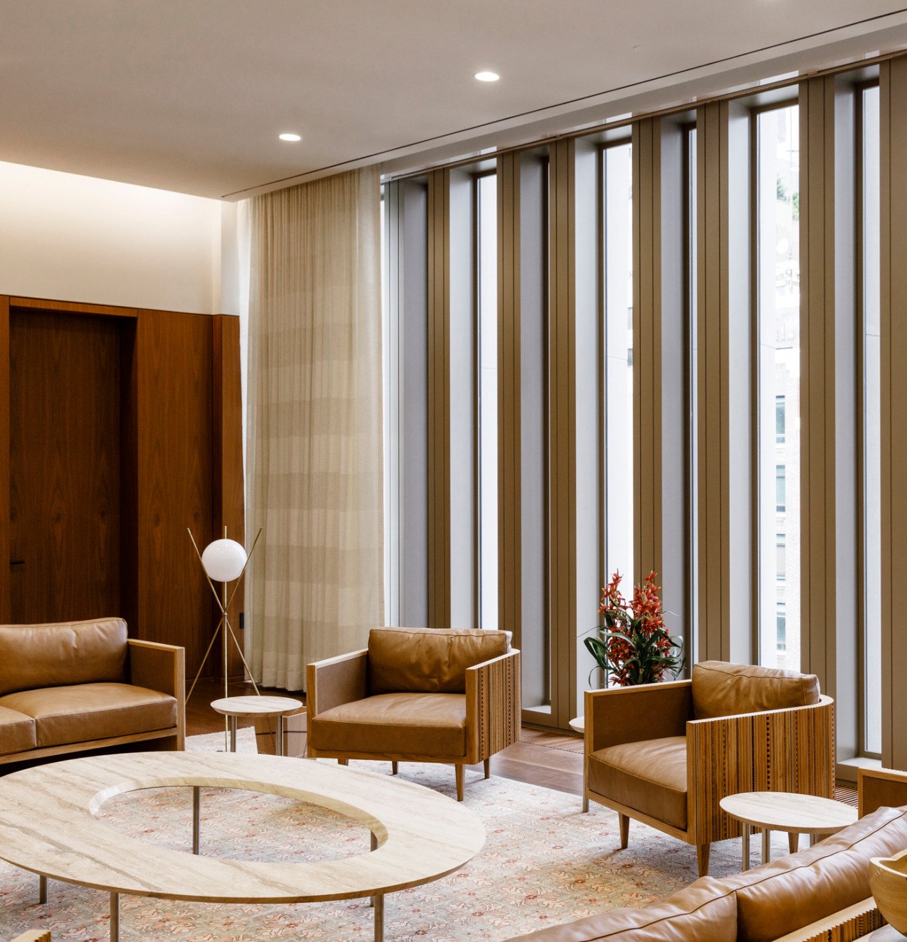 Modern interior meeting room with tan leather chairs, wooden details, and floor-to-ceiling windows overlooking a city.