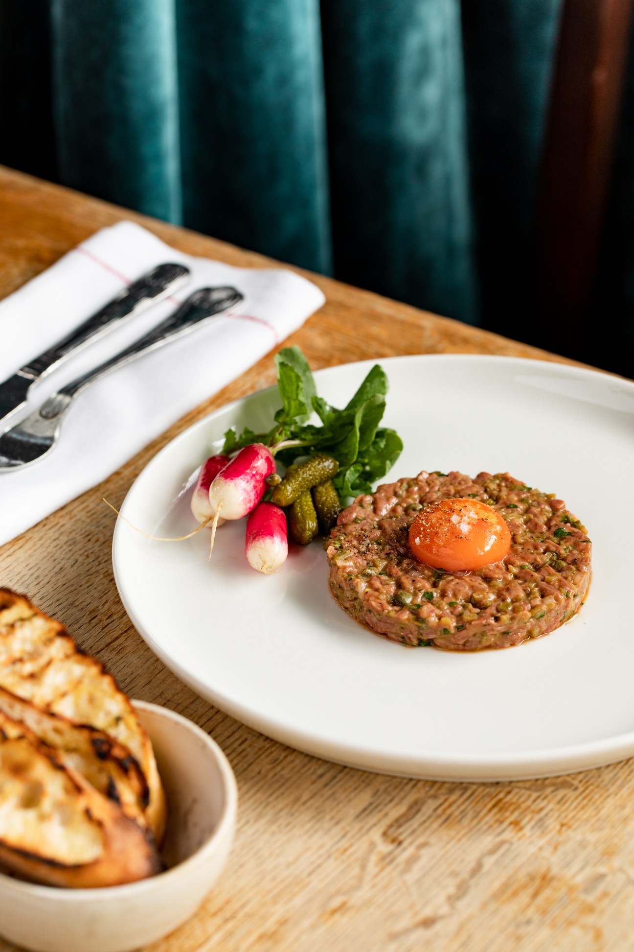 Beef tartare with egg yolk garnished with radishes, capers and greens on white plate