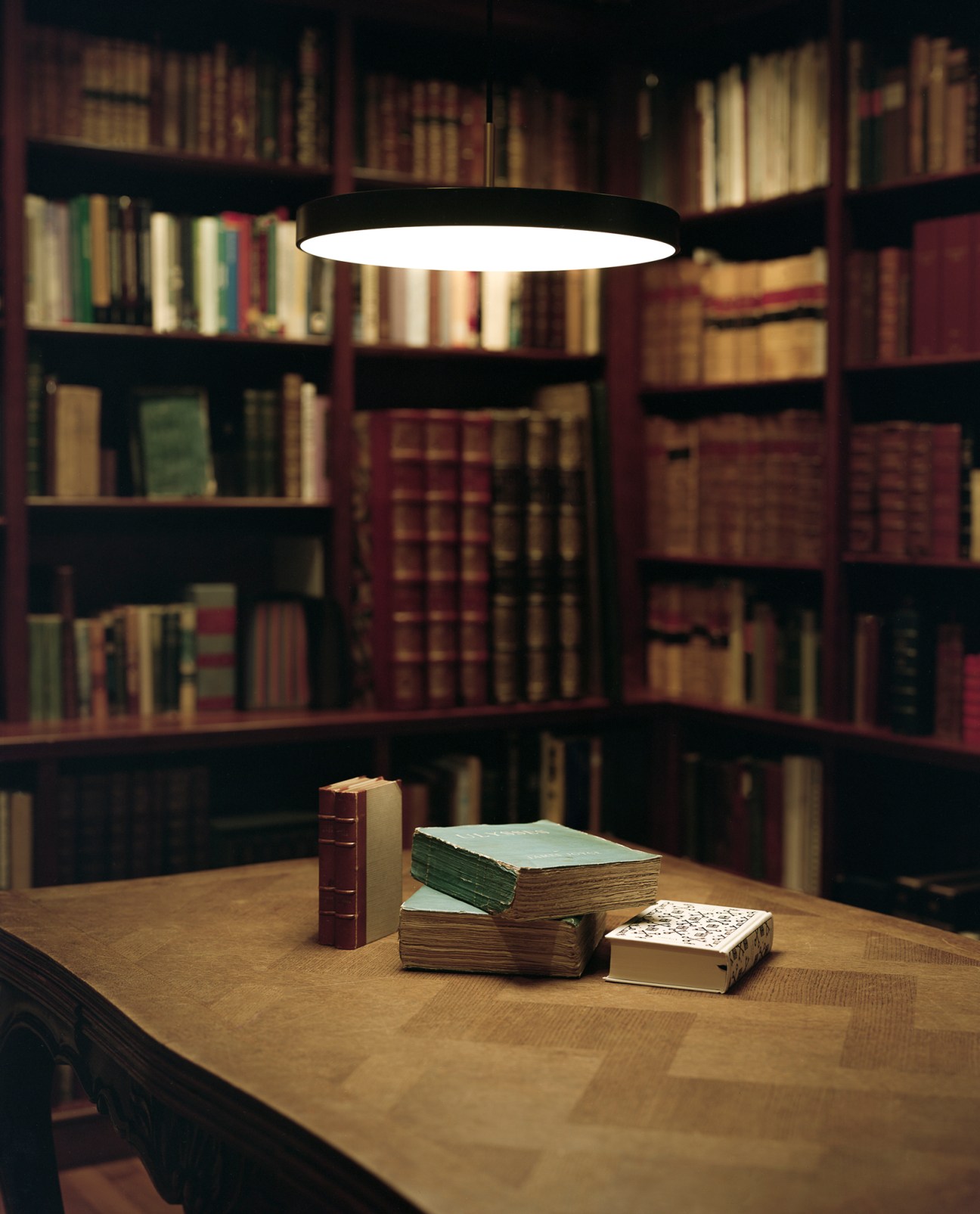 Library interior with pendant light illuminating stacked books on wooden table, surrounded by floor-to-ceiling bookshelves