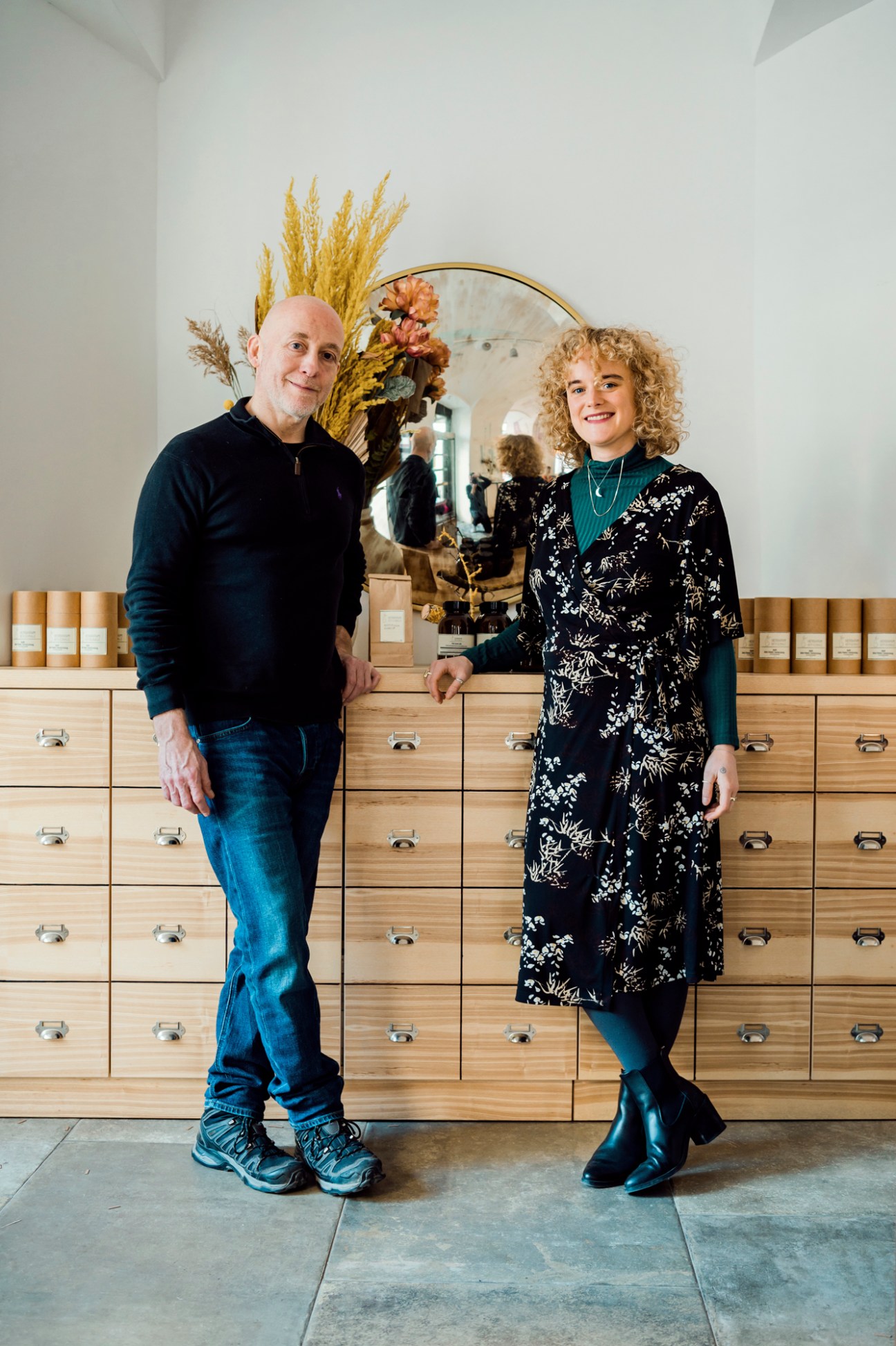 Two people standing in front of wooden drawers with herbal products in a Vienna shop