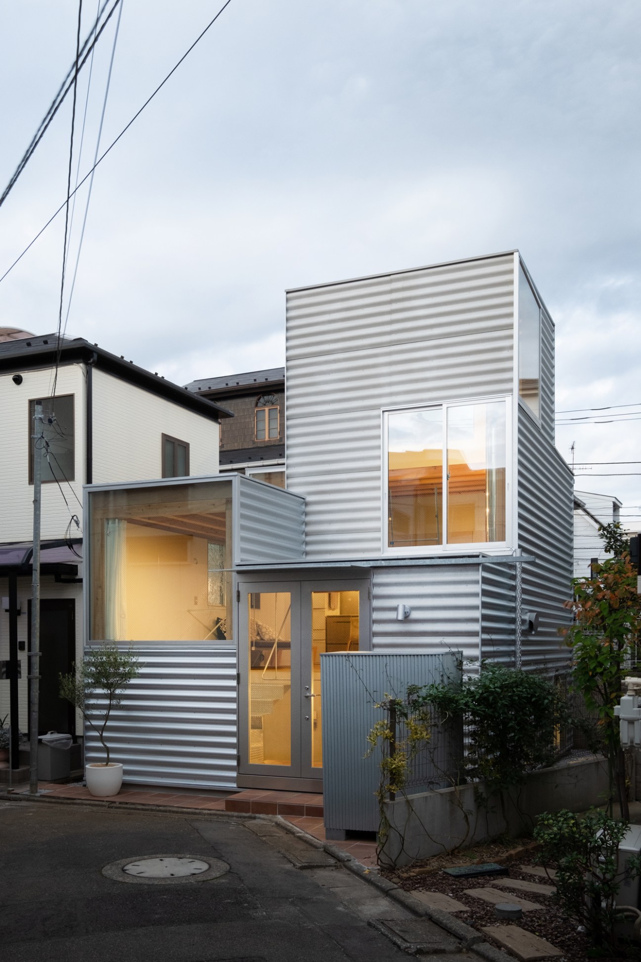 Modern Tokyo house by Unemori Architects with corrugated metal siding and large windows illuminated at dusk