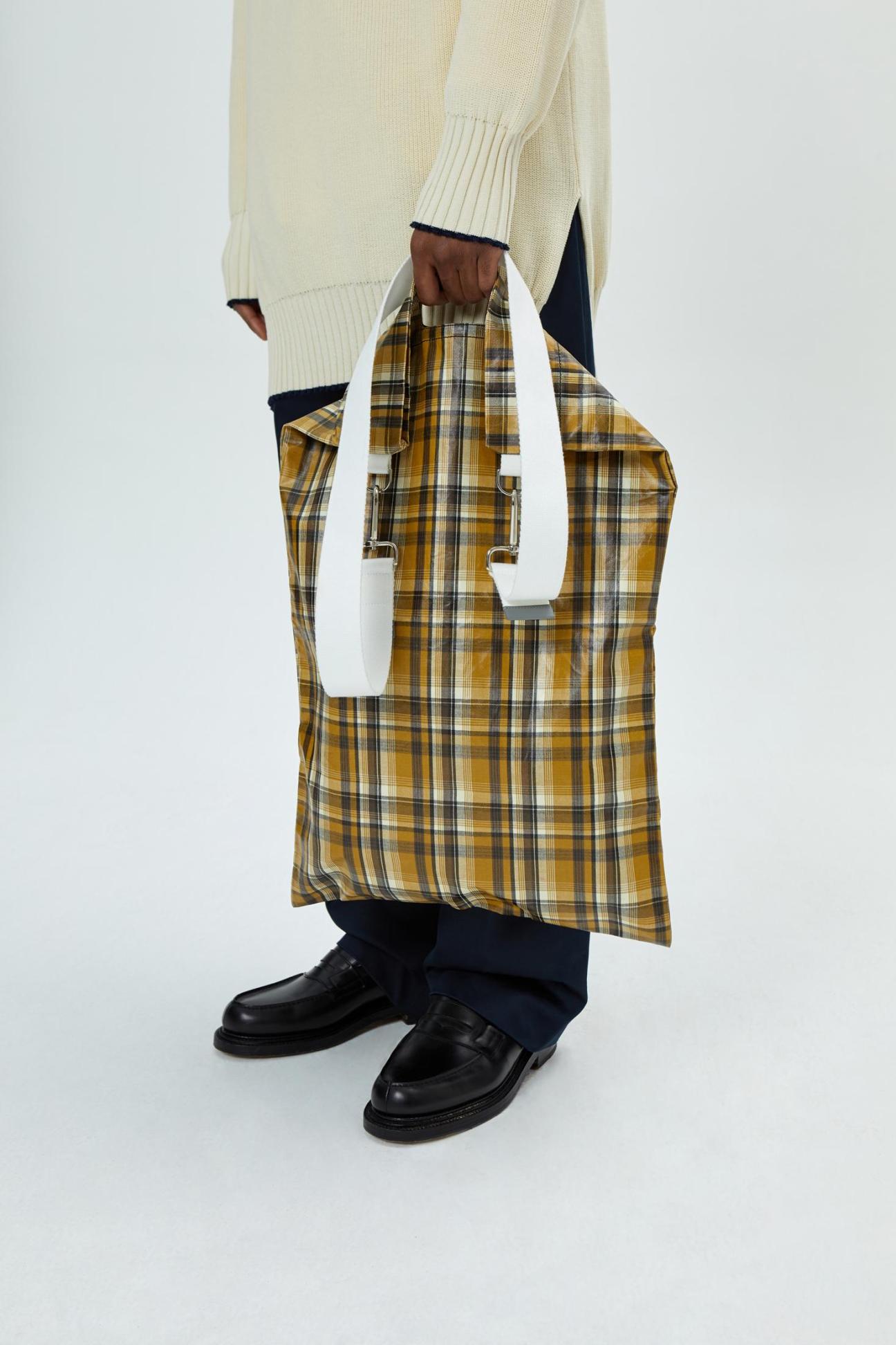 Yellow plaid tote bag with white handles being carried by person in cream sweater