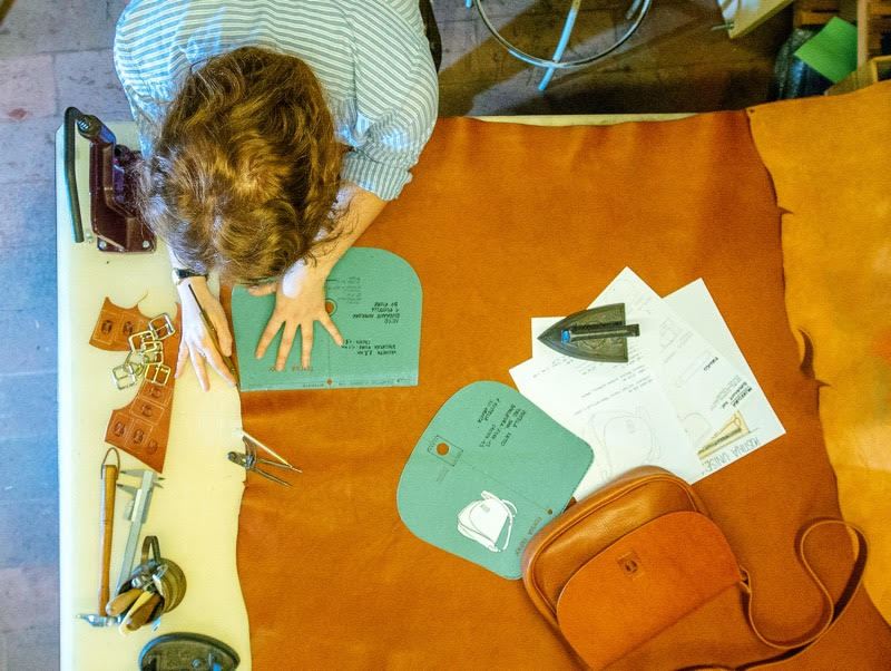 Craftsperson working on leather goods at a workshop table with patterns and materials