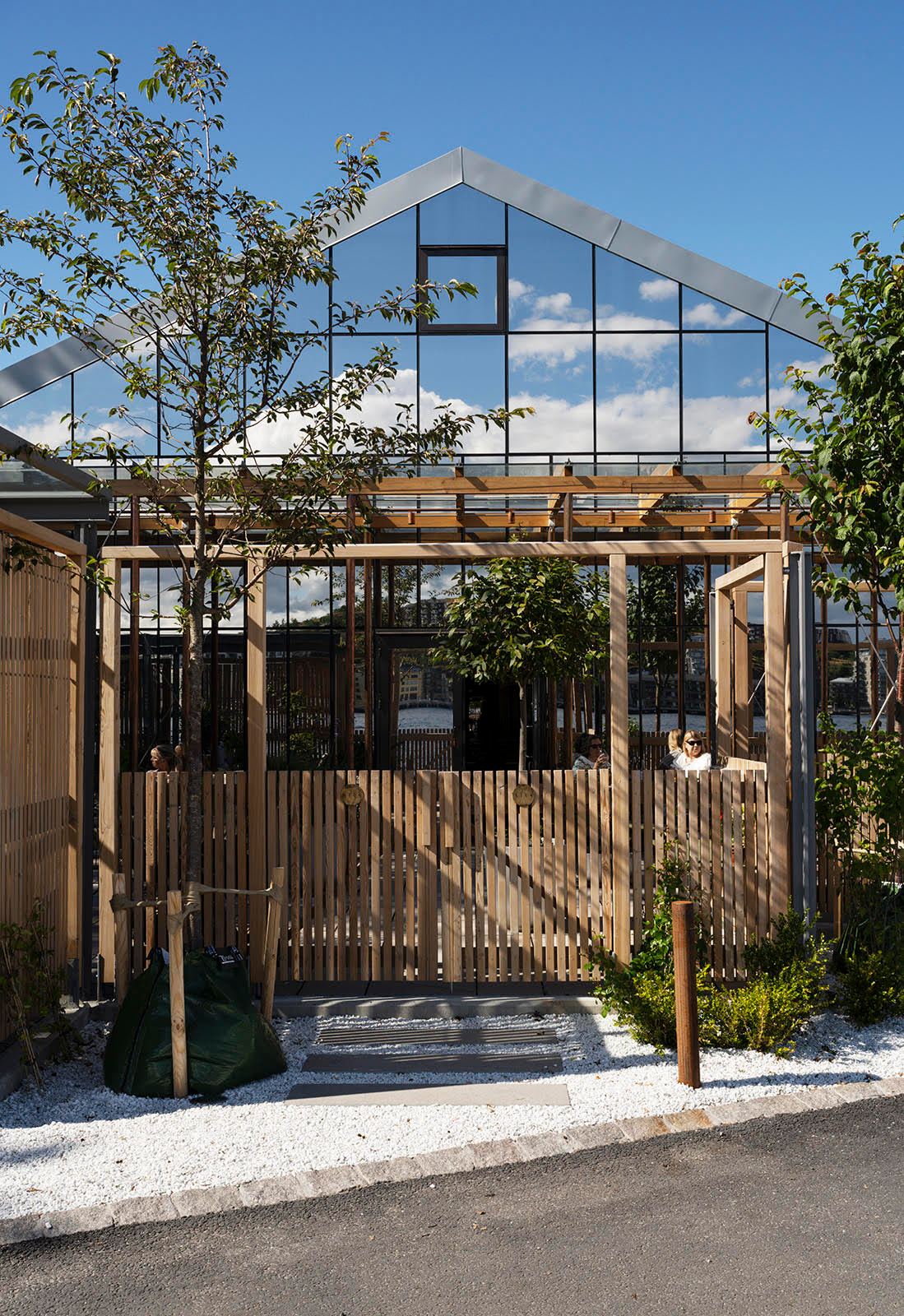 Modern glass and steel restaurant building with wooden veranda and pergola structure surrounded by trees