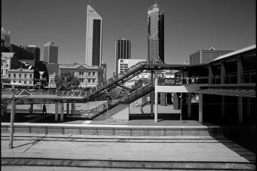 Black and white image of an elevated transit station with concrete platforms and minimal activity